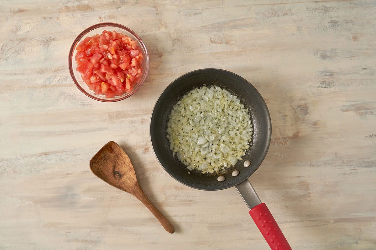 Onions and tomato pulp being cooked in a skillet until most of the liquid has evaporated for the Stuffed Tomatoes with Rice recipe, by Taste of Home.