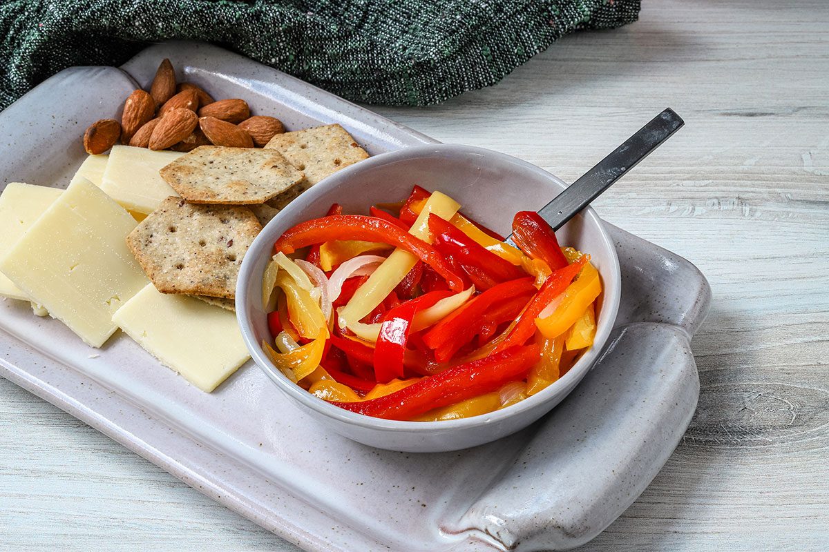 Home-canned sweet pickled peppers in a small bowl with some cheese and crackers alongside.