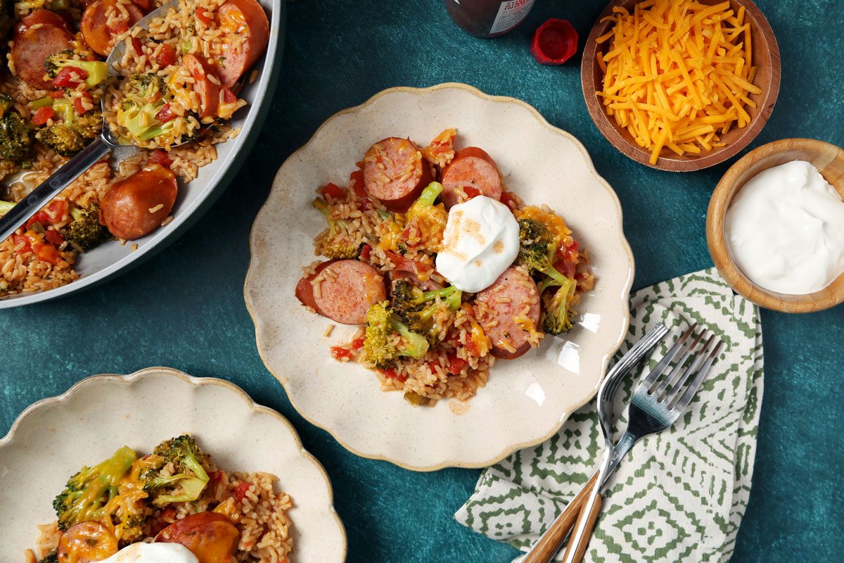 Close up of Taste of Home's Sausage, Rice and Broccoli served on beige plates on a green surface with a green linen.
