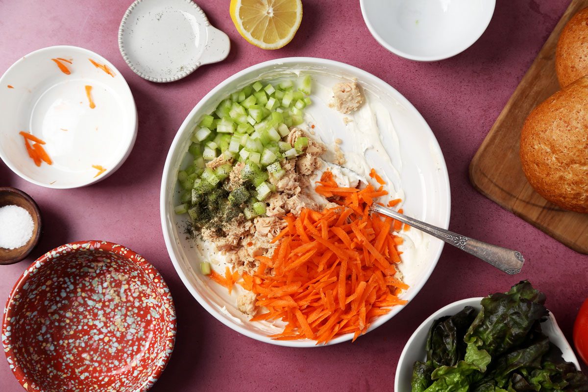 Process of making Taste of Home's salmon salad sandwich. Making the salmon salad in a large white bowl on a magenta surface.