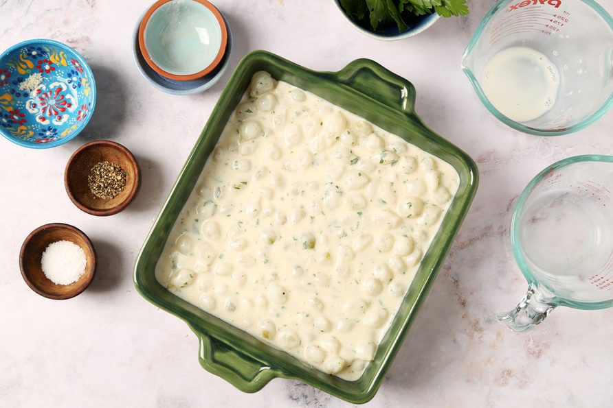 Process of making Taste of Home's Creamed Pearl Onions in a green casserole dish on a grey marble surface.
