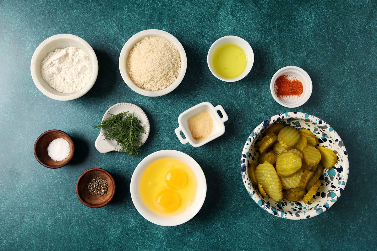 Ingredients for Taste of Home's Oven Fried Pickles laid out in small bowls on teal surface.