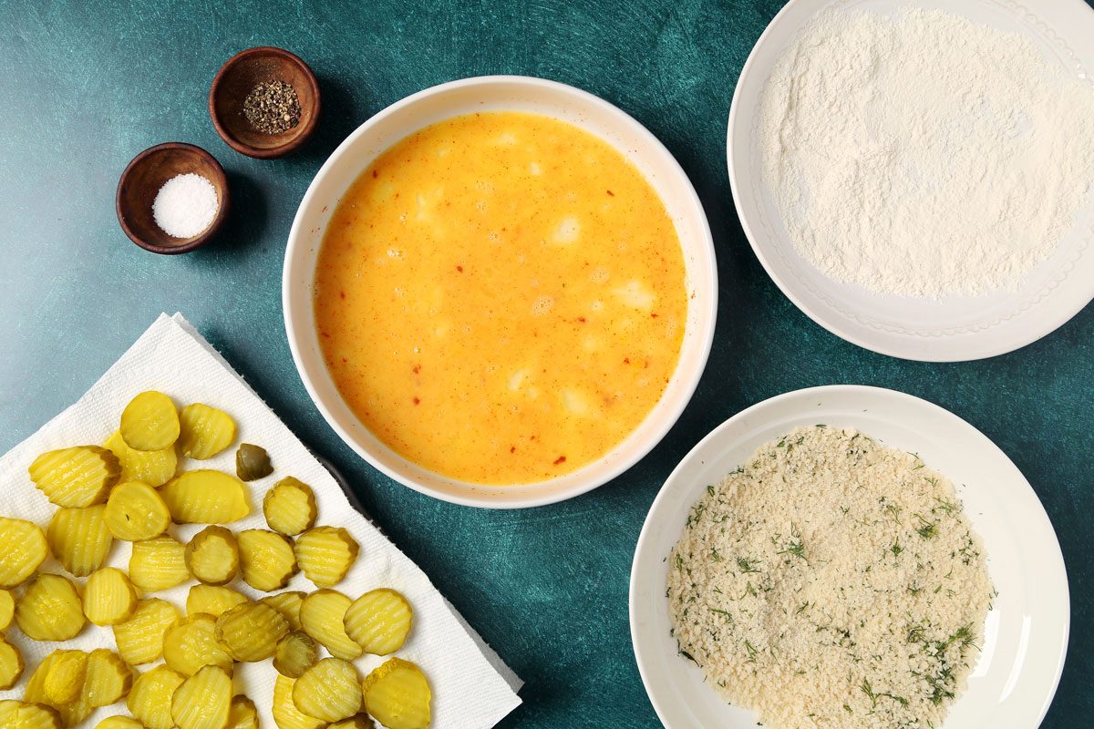 Process of making Taste of Home's Oven Fried Pickles on a wire rack and baking sheet on a teal surface.