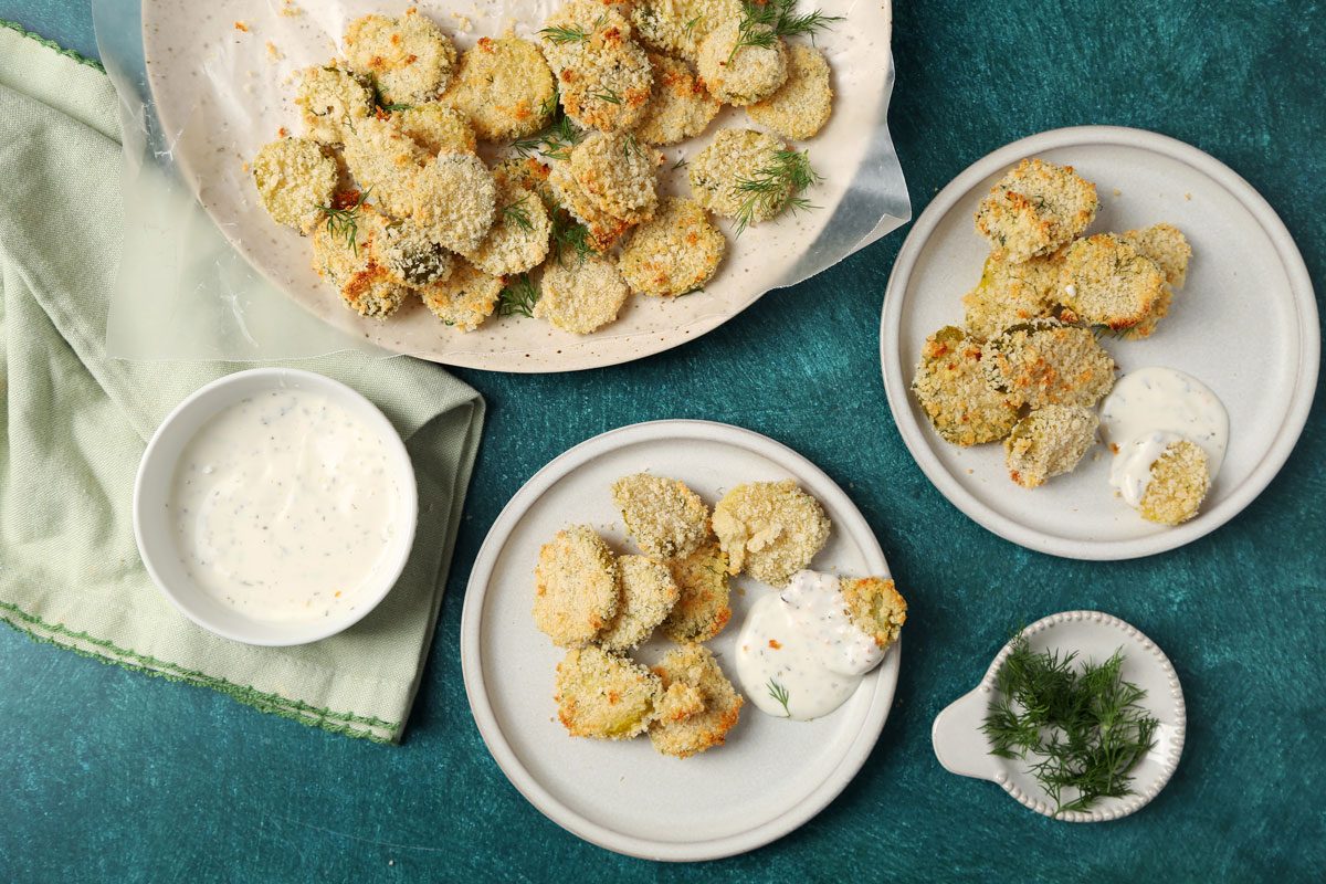 Close up of Taste of Home's Oven Fried Pickles on a plate with ranch on a teal surface.