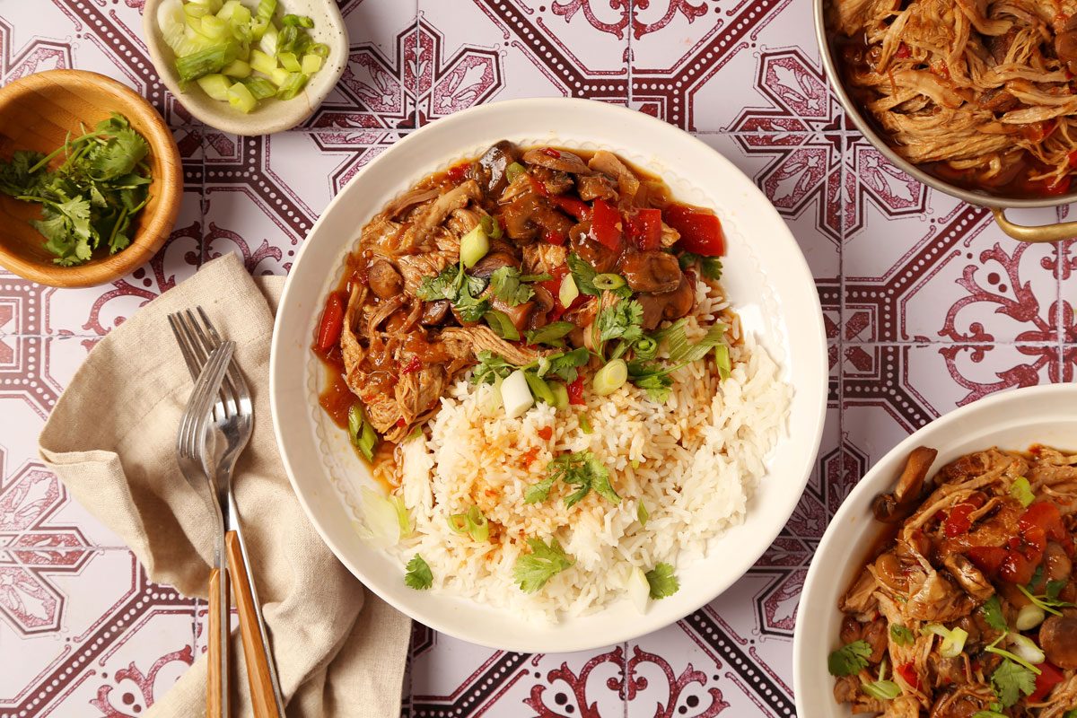 Close up of Taste of Home's Pork Bowl served with white rice in a white serving bowl on a white and red tiled surface.
