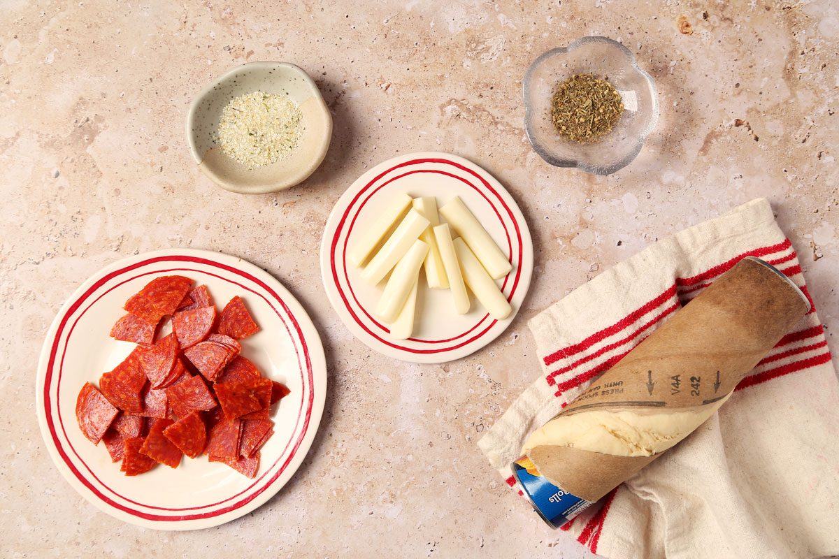 Ingredients for Taste of Home's Pepperoni Rolls laid out in small bowls on brown and beige marble surface.