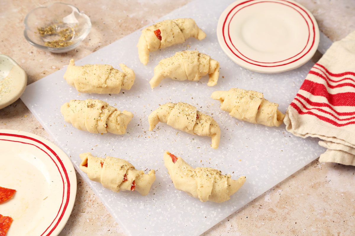 Process of making Taste of Home's Pepperoni Rolls filled and rolled on a cutting board on a brown and beige marble surface.