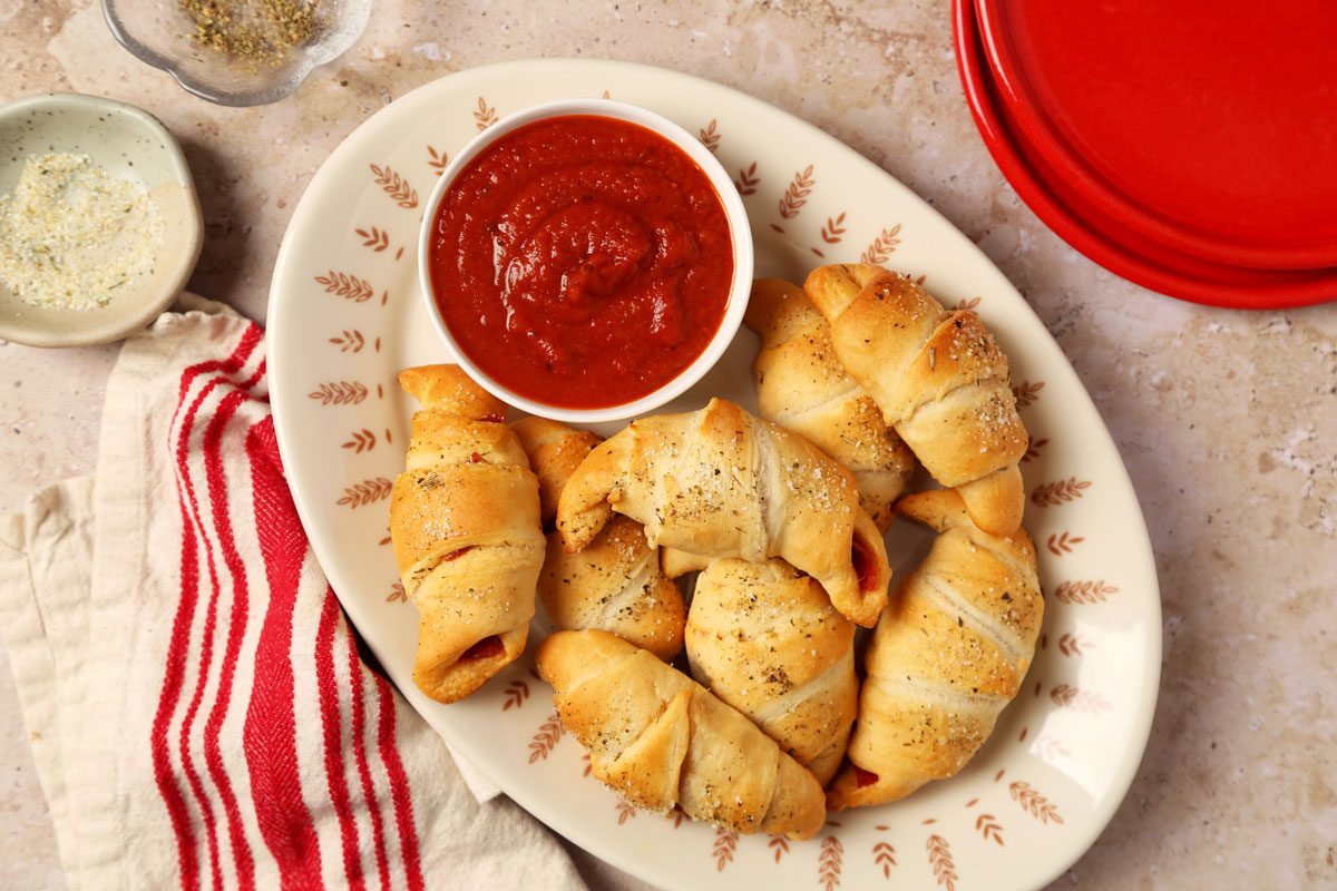 Close up of Taste of Home's Pepperoni Rolls served on a platter and red plates on a brown and beige marble surface.