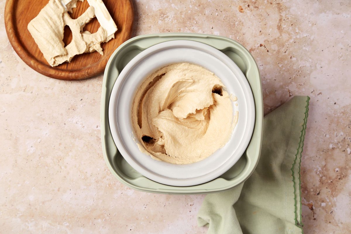 Process of making Taste of Home's Peanut Butter Ice Cream in an ice cream maker on a brown marble surface.