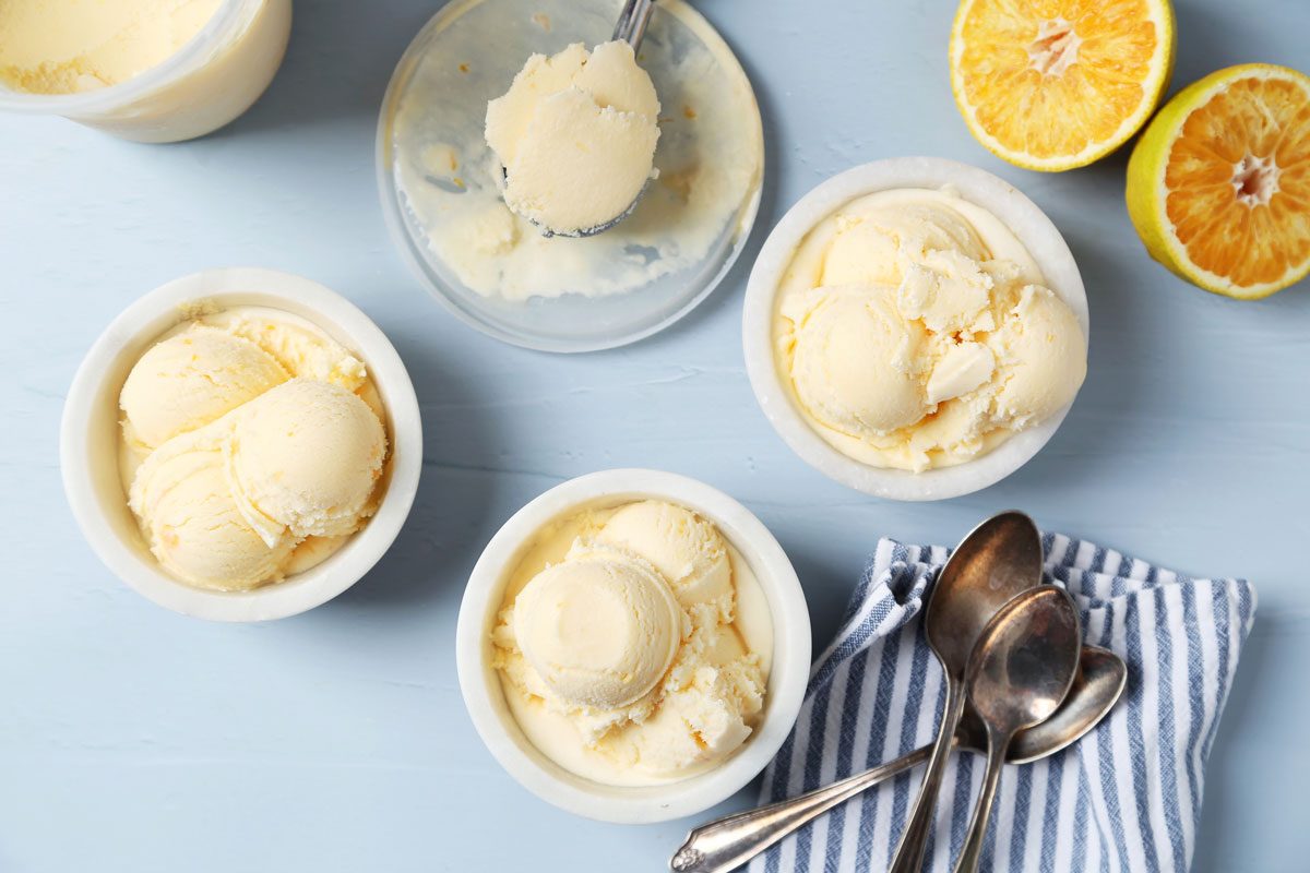 Close up of Taste of Home's Orange Sherbet served in white bowls on a white marble surface with an orange towel.