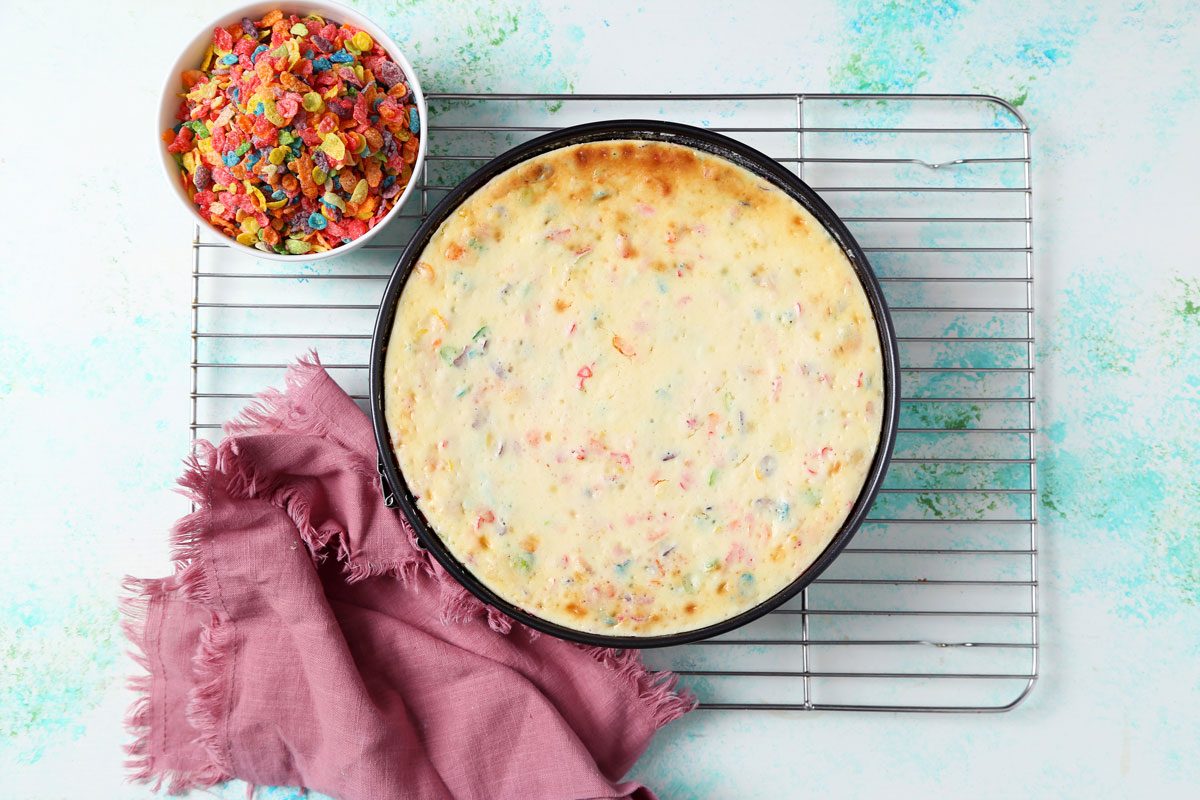 Process of making Taste of Home's Fruity Pebbles Cheesecake being cooled on a wire rack.