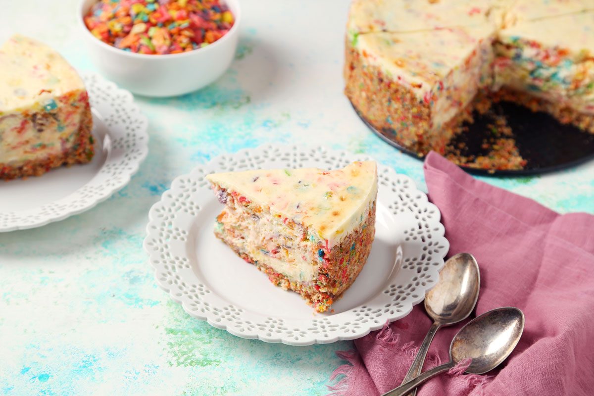 Close up of Taste of Home's Fruity Pebbles Cheesecake sliced and served on a white plate.