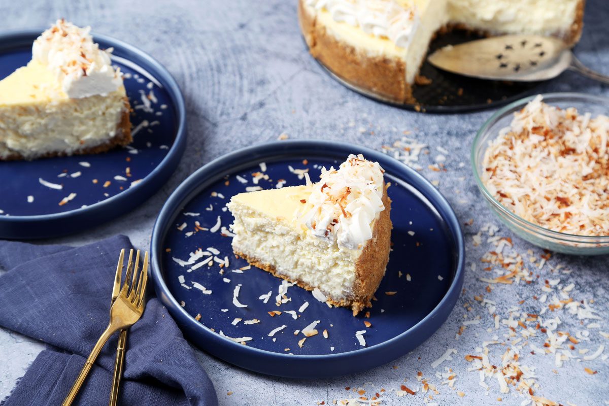 Close up of Taste of Home's Coconut Cheesecake served on blue plates on a dark blue surface.