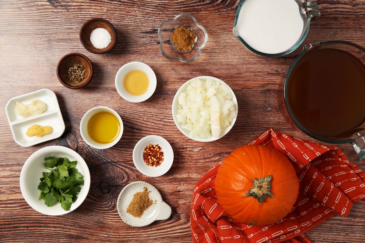 Ingredients for Taste of Home's Chicken Pumpkin Soup laid out in small bowls on a brown wooden surface.