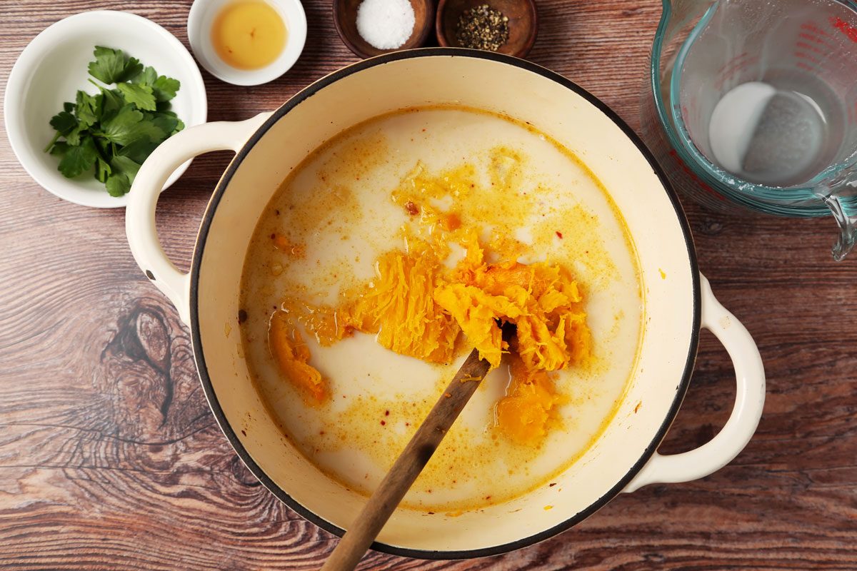 Process of making Taste of Home's Chicken Pumpkin Soup in a dutch oven on a brown wooden surface.