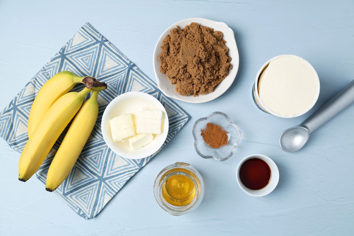 Ingredients for Taste of Home's bananas foster laid out in small bowls on a light blue surface and a blue kitchen towel.