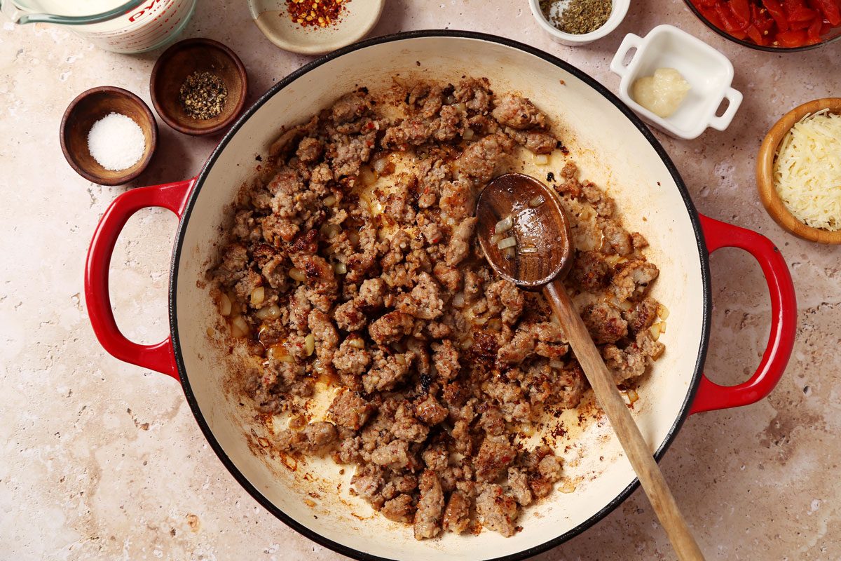 Process of making Taste of Home's Sausage and Bow Tie Pasta laid in a large red dutch oven on a brown marble surface.