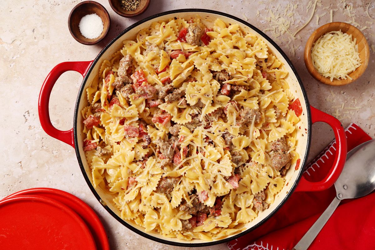 Close up of Taste of Home's Sausage and Bow Tie Pasta in a large dutch oven with parmesan cheese on a brown marble surface.