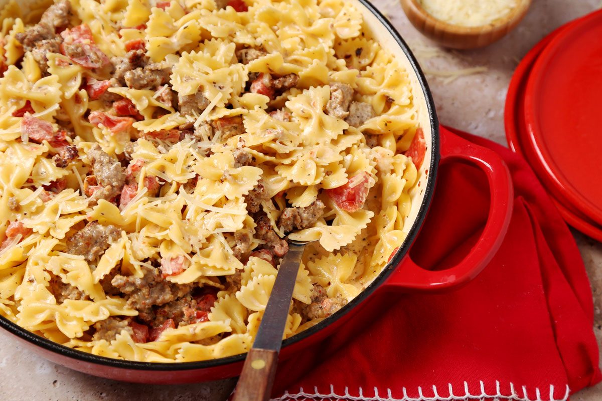 Close up of Taste of Home's Sausage and Bow Tie Pasta in a large dutch oven with parmesan cheese on a brown marble surface.
