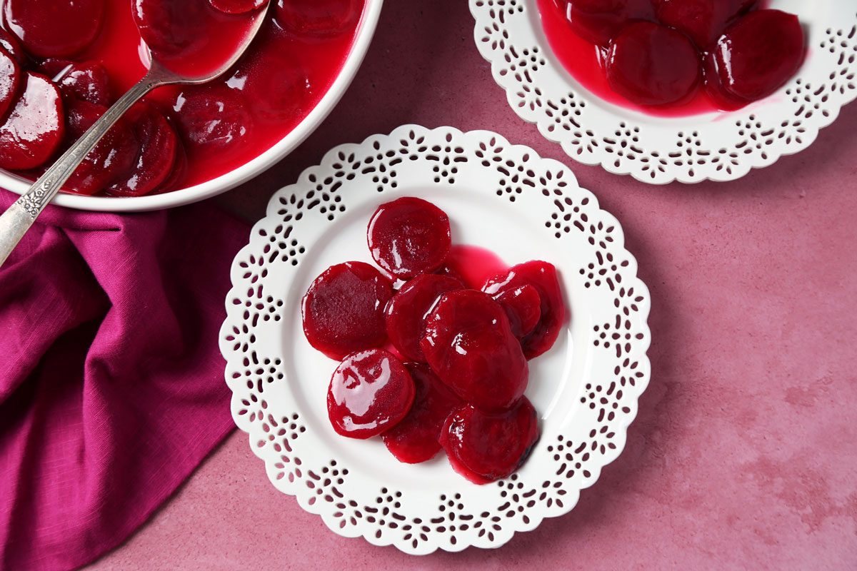 Close up of Taste of Home's Harvard Beets served on white plates on a magenta surface.
