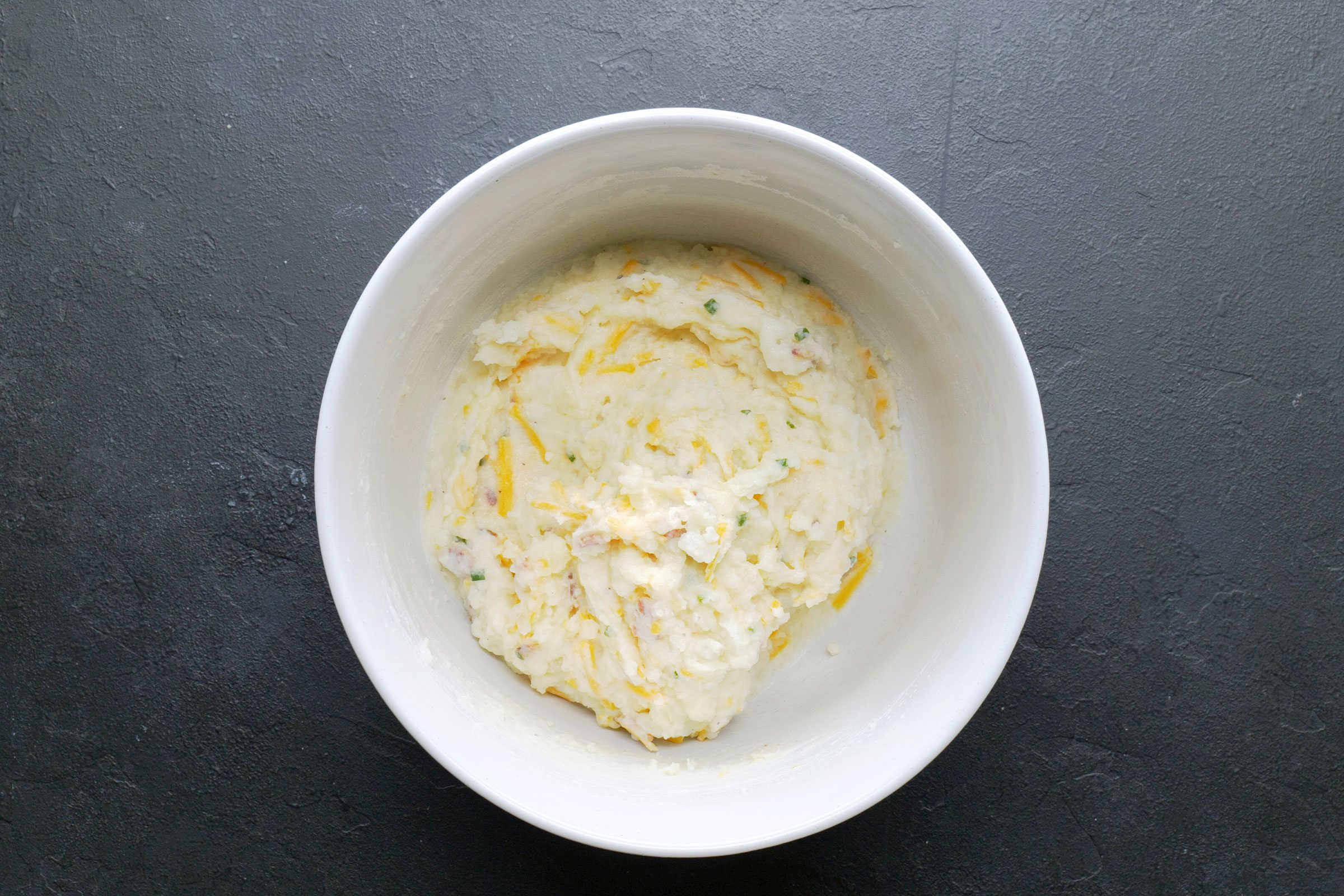 Stirred in milk, bacon, onion, chives, salt, pepper and 1 cup cheese in potato pulp