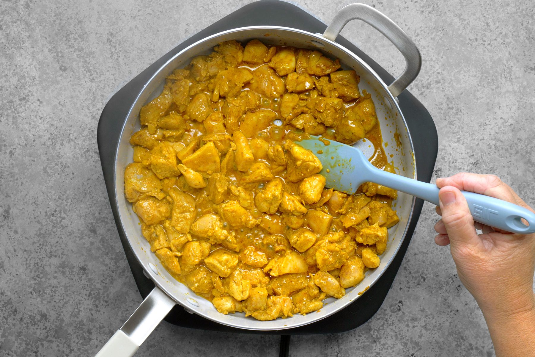 Marinated chicken is being sautéed in a skillet, sizzling as it cooks. The vibrant pieces of chicken are evenly coated in a rich marinade, releasing savory aromas into the air.