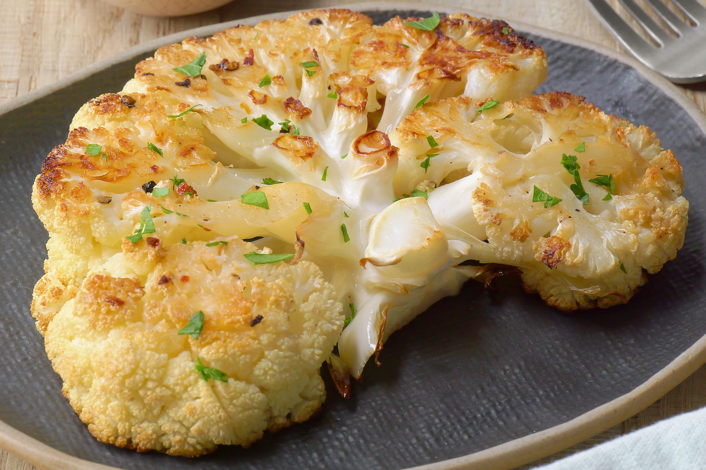 Cauliflower Steak sprinkled with parsley and placed on a grey dish