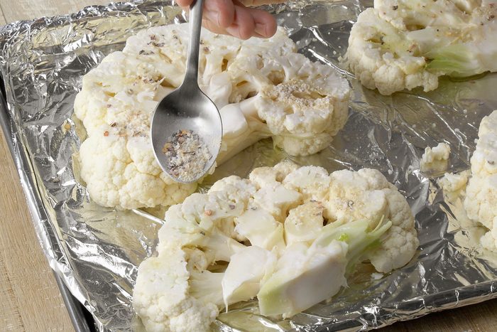 Sprinkling seasoning mixture over cauliflower slices
