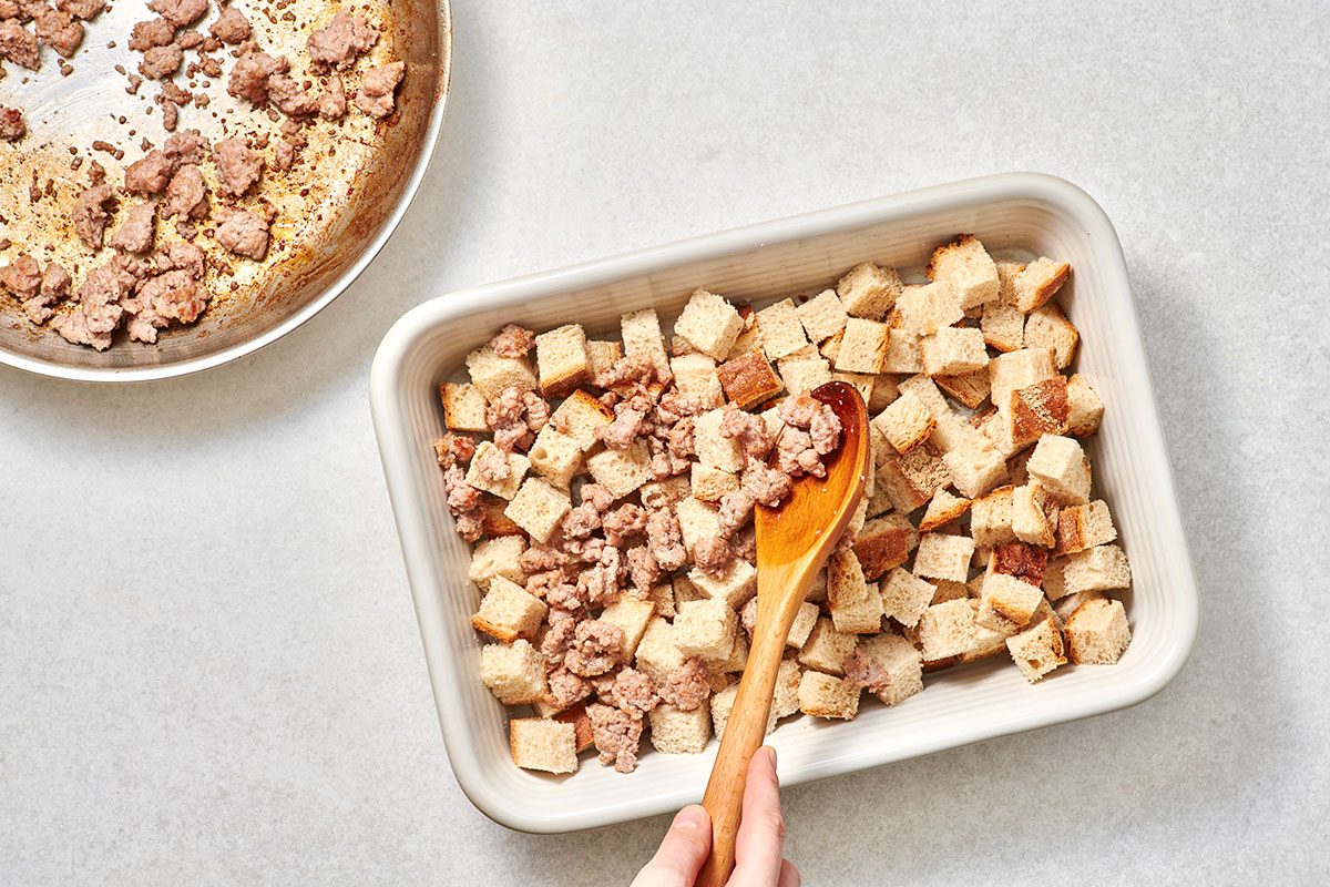 Layering cooked sausages in a baking dish with cubed bread