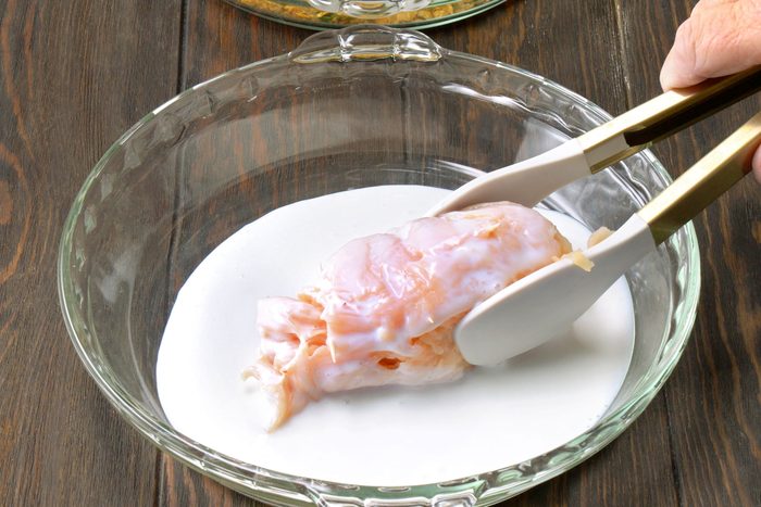 Dipping chicken breast roll in buttermilk in a shallow bowl