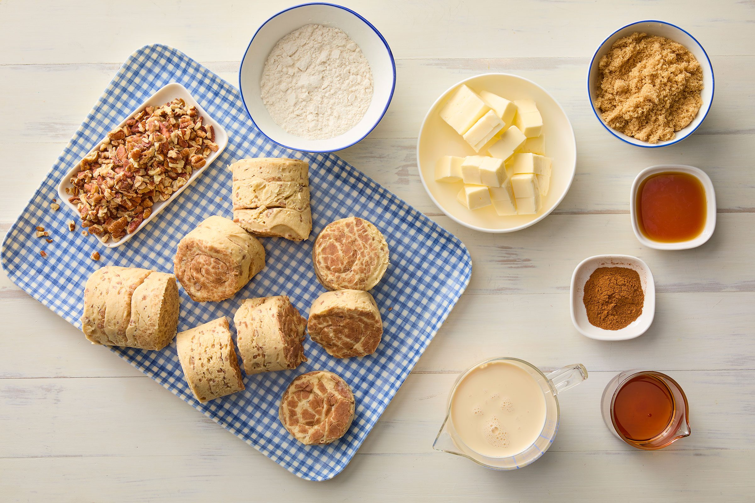 Cinnamon rolls, milk, maple syrup, vanilla extract, all purpose flour, brown sugar, butter, pecans and icing packets on a tray and in small bowls
