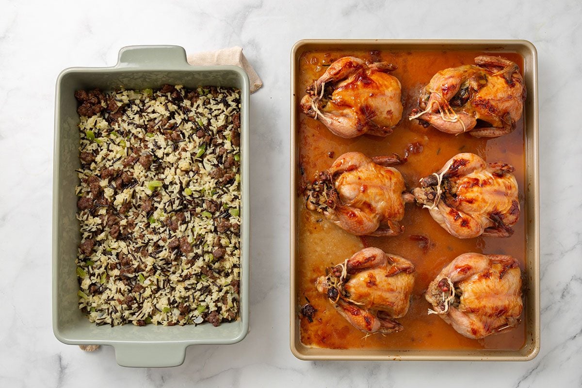 Baked stuffing mixture in a baking dish next to a baking pan of cooked cornish hens topped with apricot sauce for step five of Cornish Game Hens with Wild Rice Stuffing recipe for Taste of Home