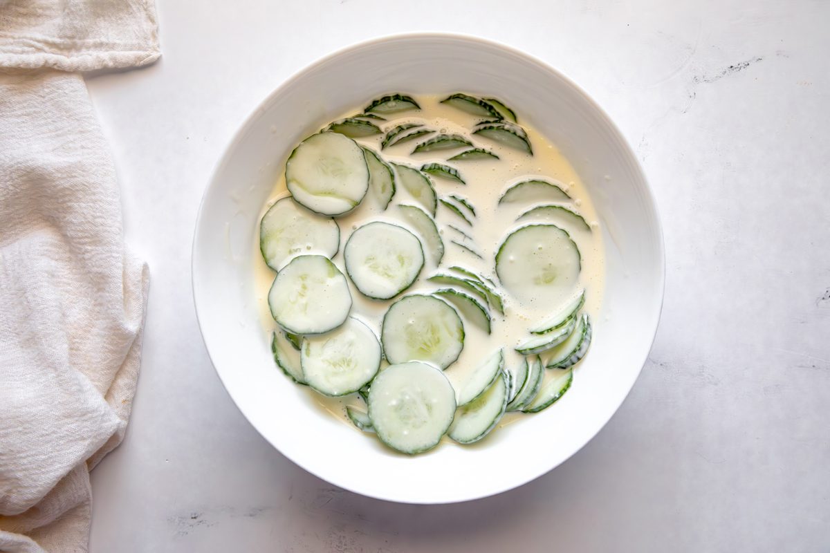 Overhead shot for Taste of Home Creamy Cucumber Salad, dressing poured over cucumbers in a large bowl after chilling.