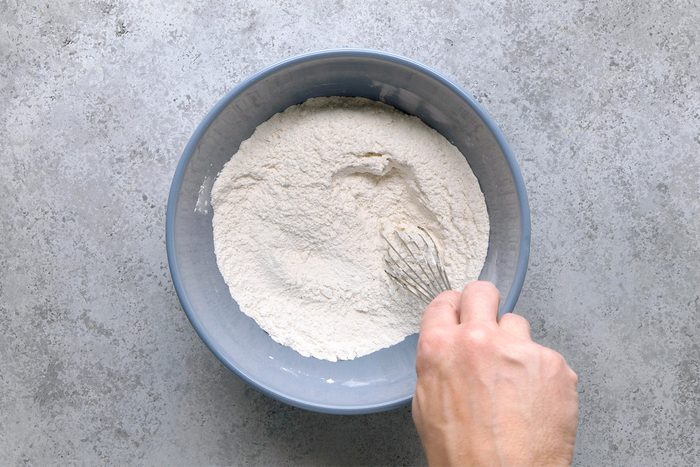 Overhead shot of a large bowl; whisk flour; baking powder; sugar and salt; grey surface;