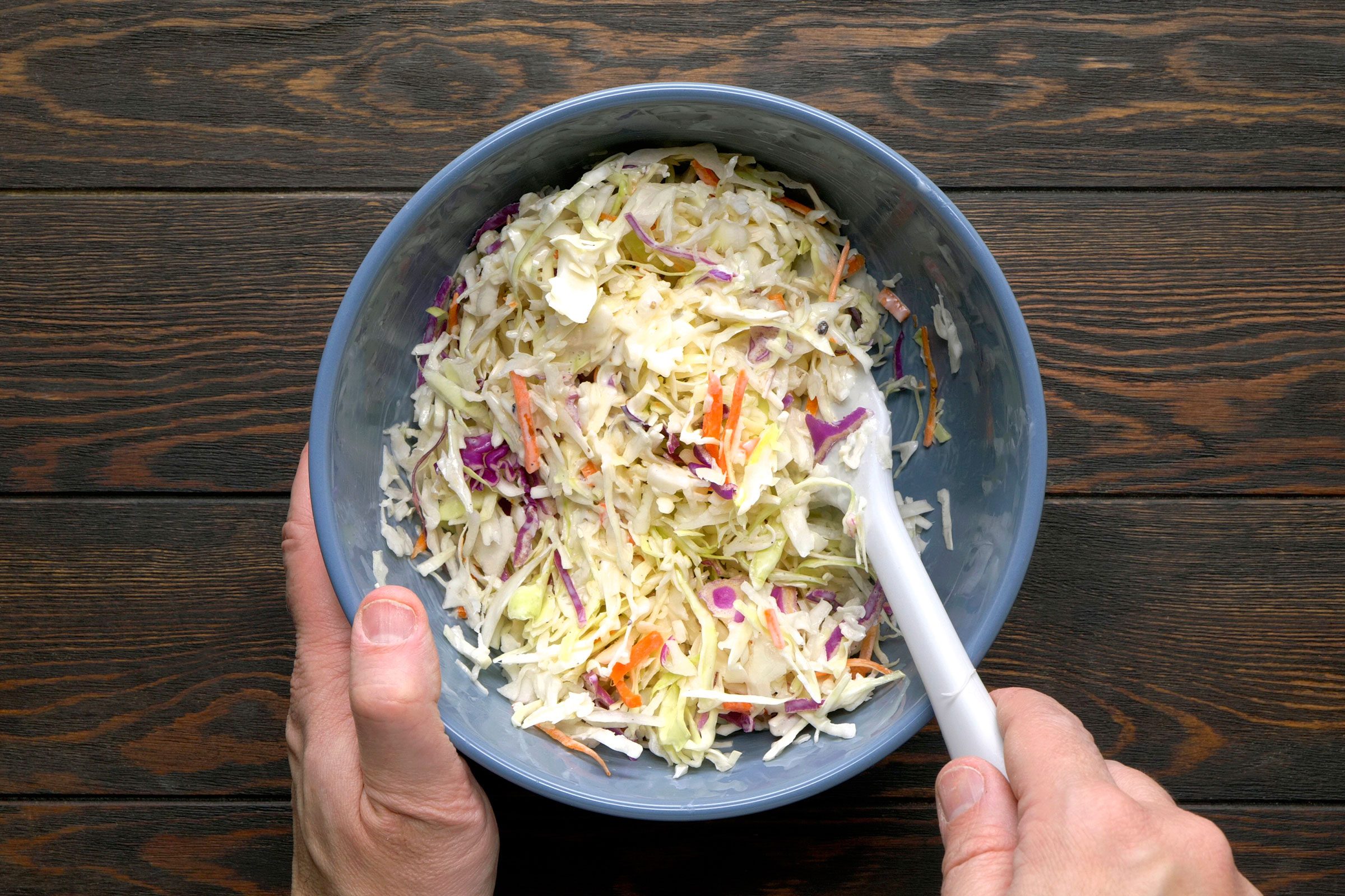 Making coleslaw by mixing ingredients in a blue bowl