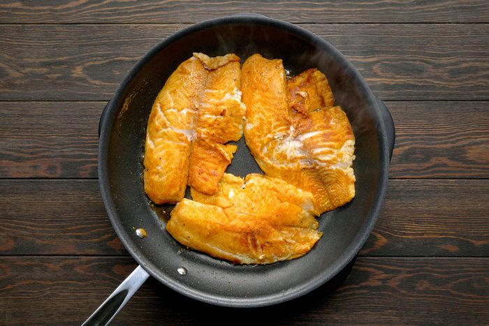 Cooking flour and seasonings coated fish in a large skillet