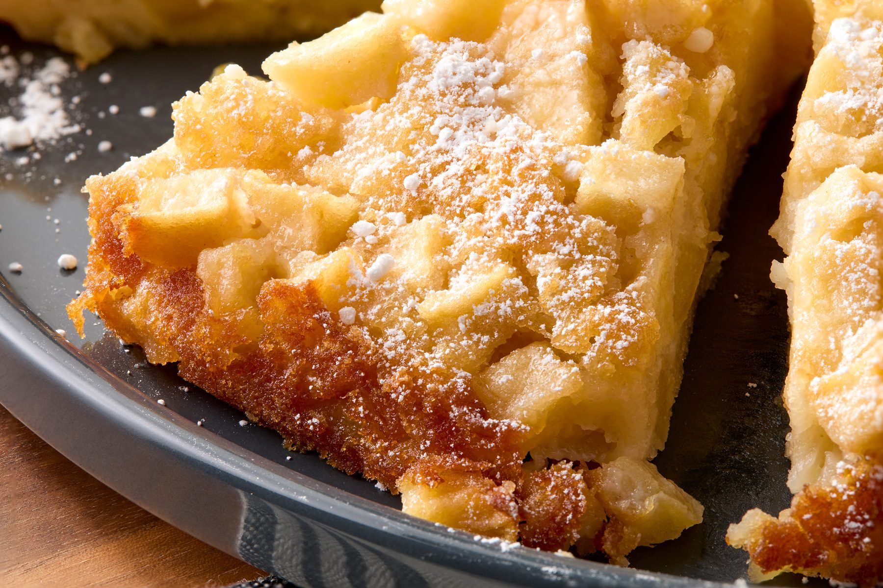 Close-up horizontal image of a slice of apple cake on a black plate.