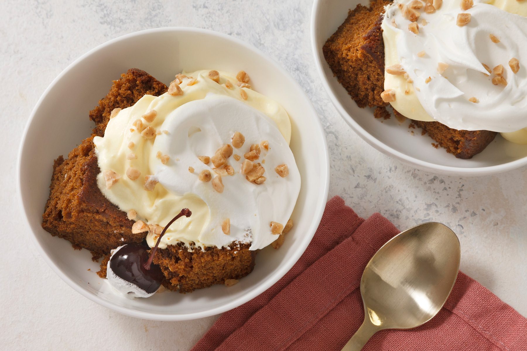 Table view shot of Gingerbread Trifle; garnish with cherries; serve in bowls; spoon; napkin; marble surface.