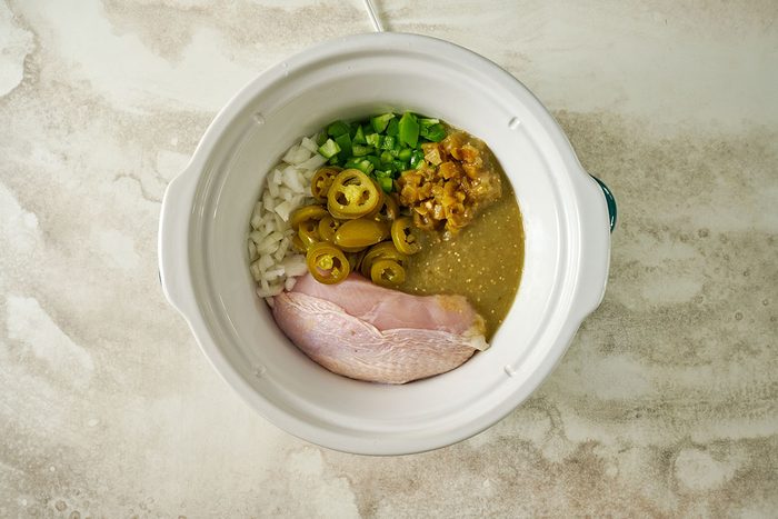 Overhead view of chicken breasts, onions, green peppers, pickled jalapenos, and green chiles arranged in a slow cooker with salsa verde poured over for the Taste of Home Green Chicken Chili recipe.