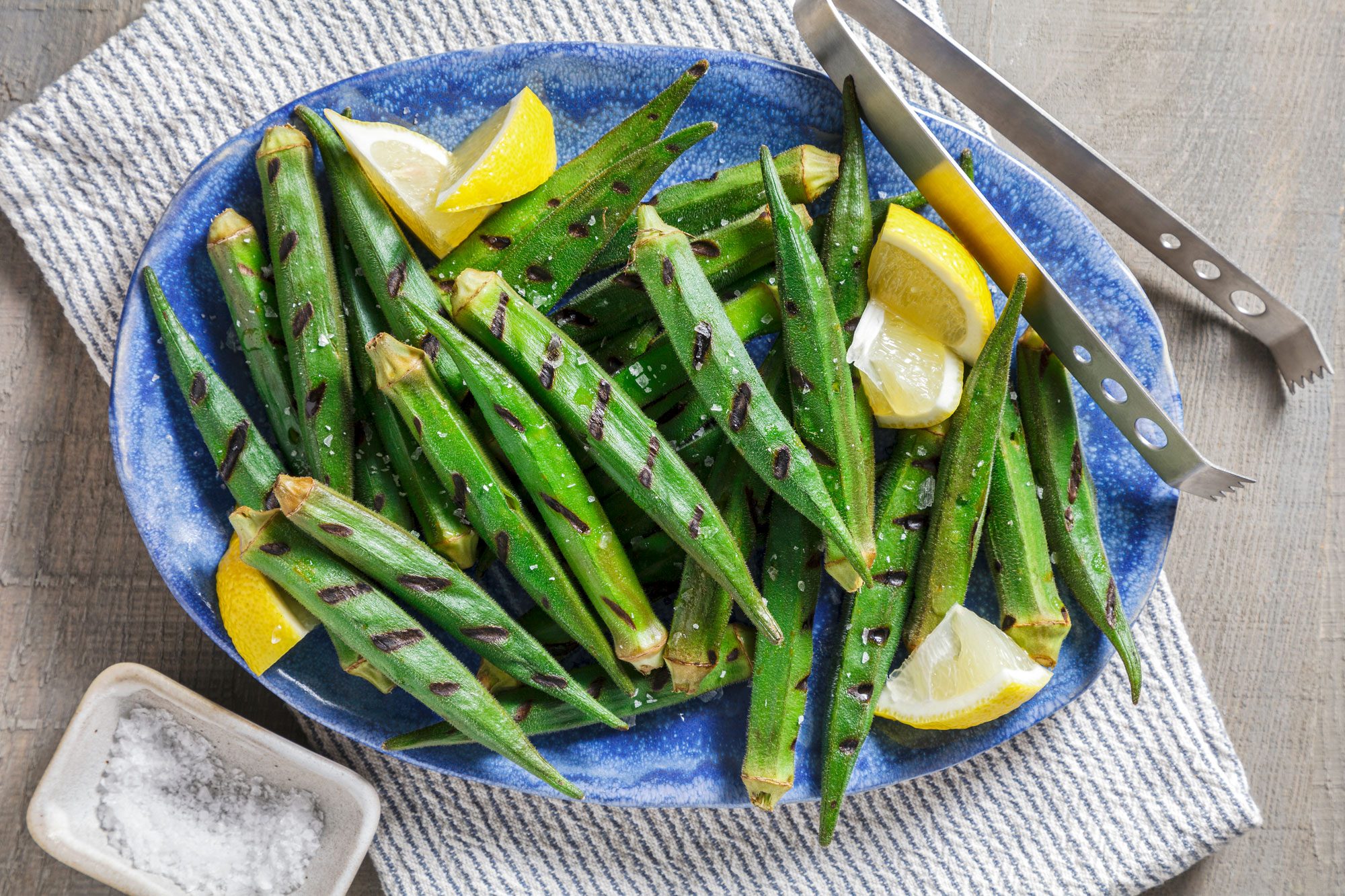 Overhead shot; remove grilled okra from skewers and place on a platter; garnish with lemon juice and salt; serve hot; napkin; wooden surface;