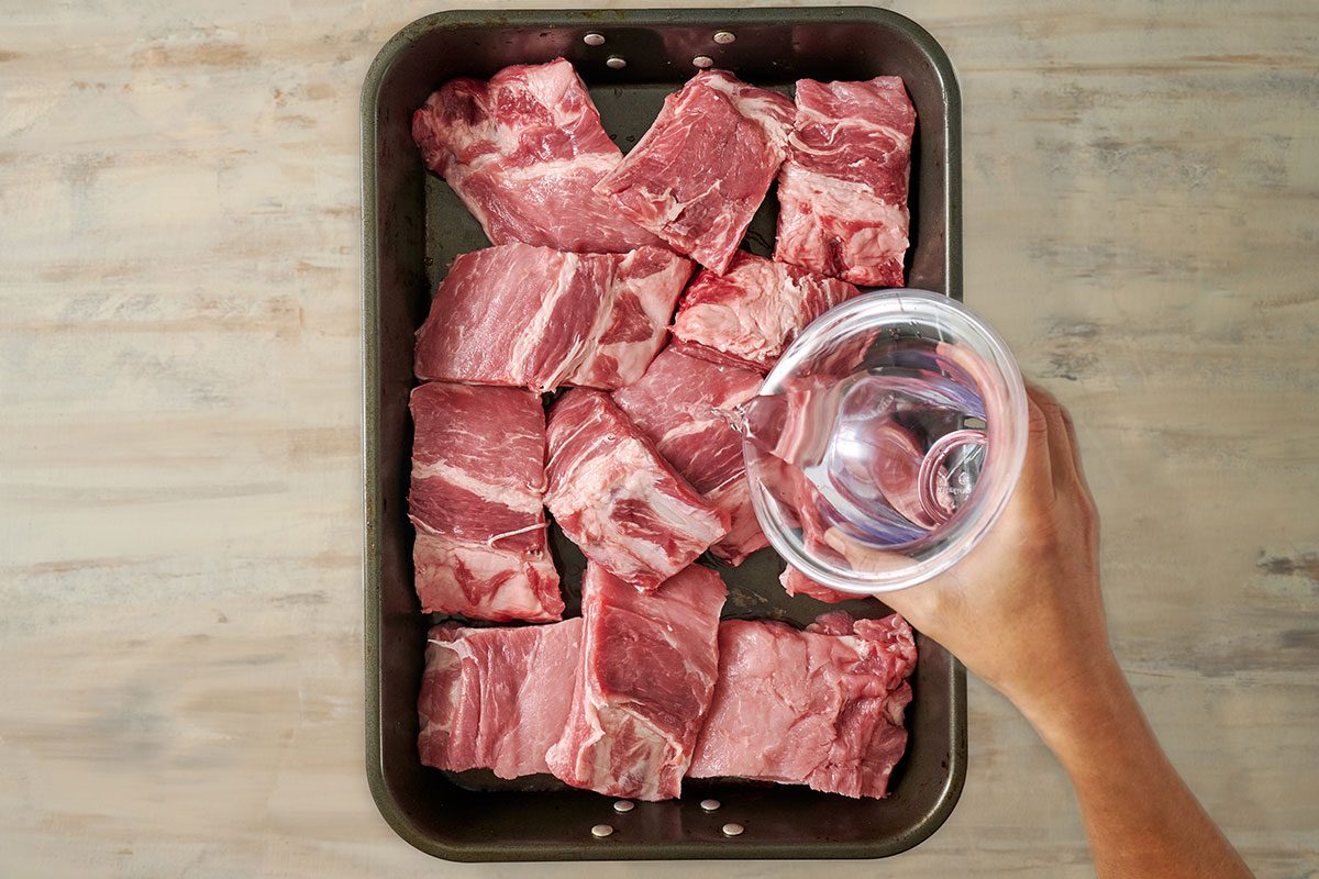 Overhead view of pork baby back ribs in a roasting pan with water poured over, covered with aluminum foil, and ready to bake for the Taste of Home Honey Garlic Ribs recipe.