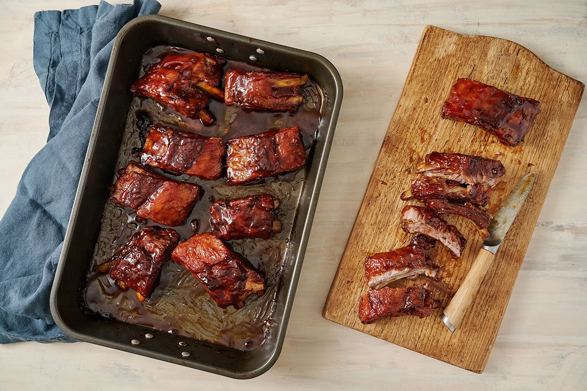 Overhead view of baked ribs resting in a roasting pan, with individual pieces sliced and ready to serve for the Taste of Home Honey Garlic Ribs recipe.