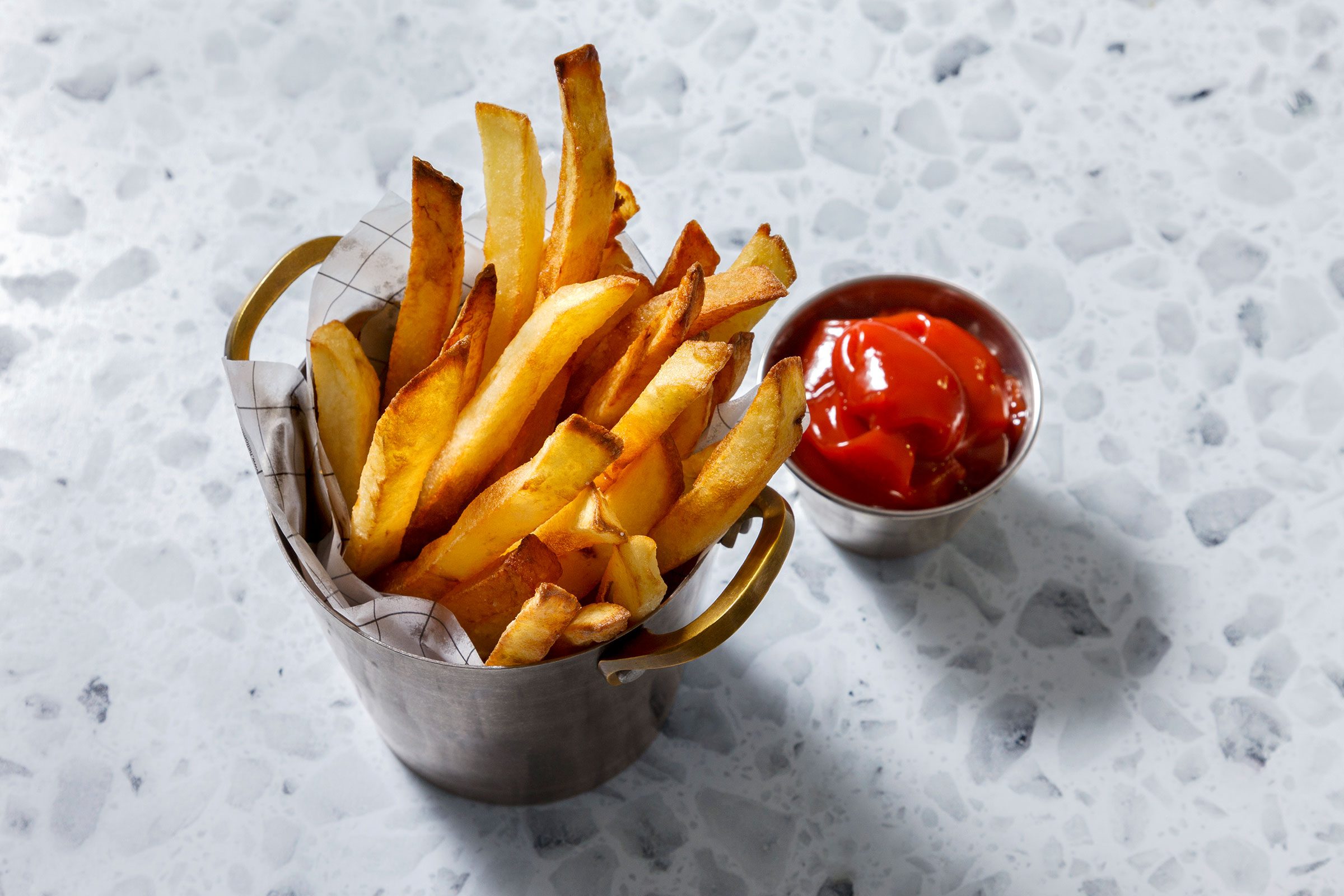 Pan fried french fries in a metal utensil with ketchup on side