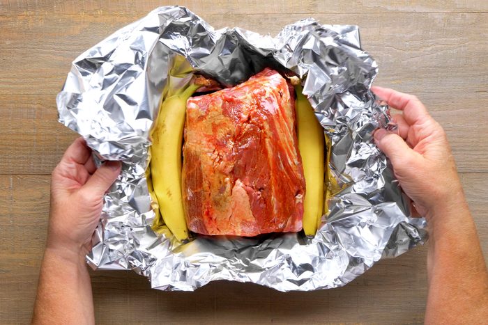 Seasoned pork meat with bananas on side in a foil sheet
