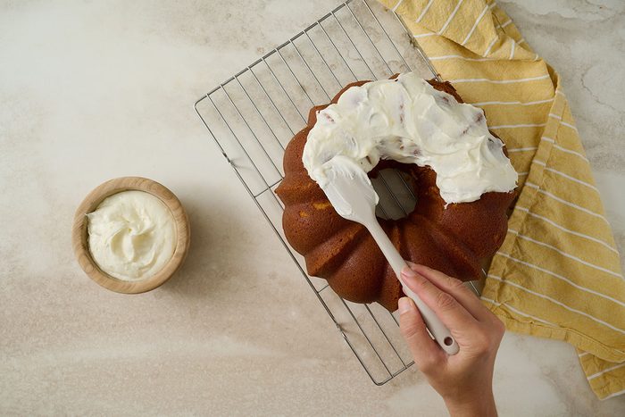 Overhead view of lemon frosting being spread over the cooled Taste of Home Lemon Pound Cake, which rests on a wire cooling rack.