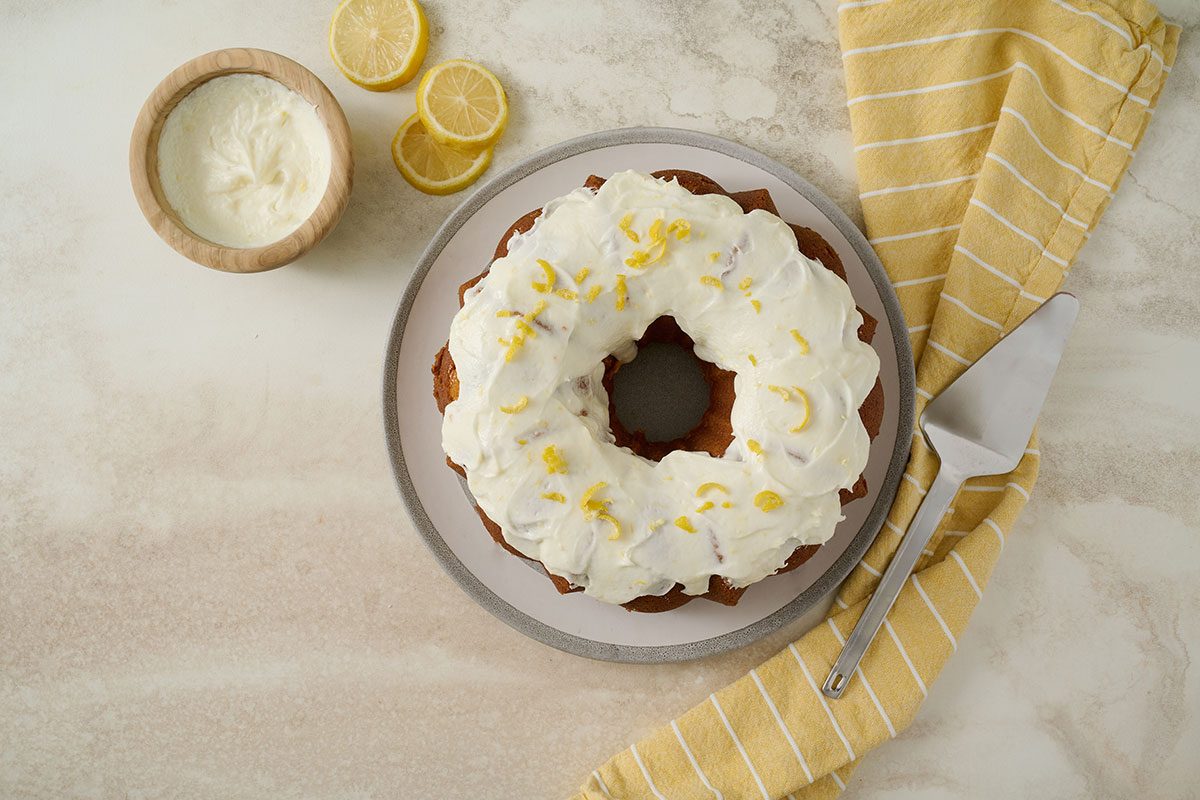 Overhead hero shot of the finished Taste of Home Lemon Pound Cake, topped with lemon frosting and garnished with extra lemon zest, served on a cake stand.