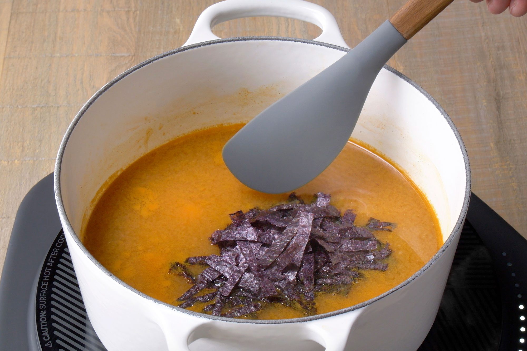 Close shot of add tofu; miso and wakame; simmer another 2-3 minutes; induction; wooden surface;