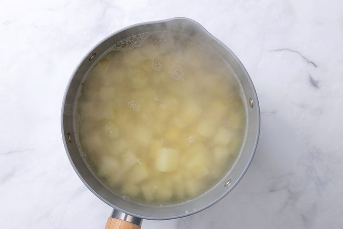 Cubed potatoes in boilling water in a saucepan for step two of Onion Mashed Potatoes recipe for Taste of Home