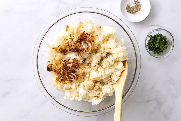 Mashed potatoes in a mixing bowl and seasoned with salt, pepper, and caramelized onion for Onion Mashed Potatoes recipe for Taste of Home
