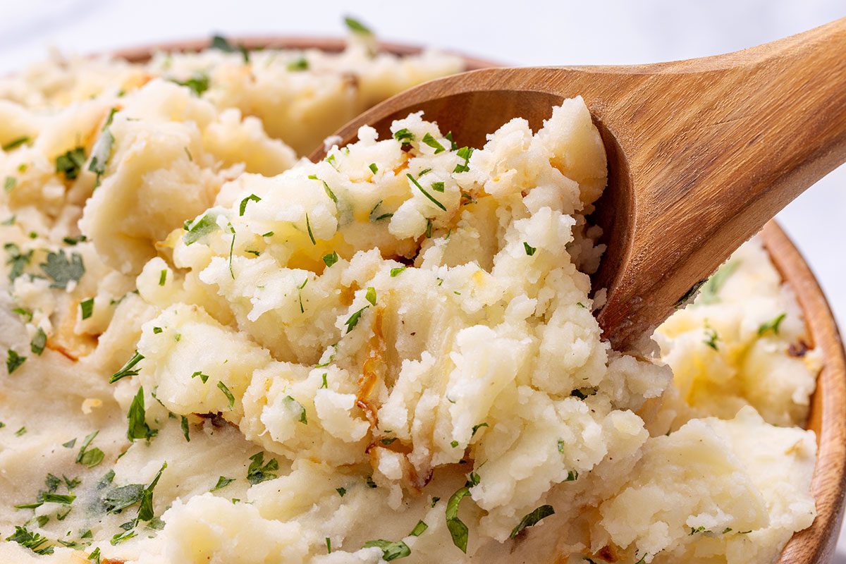Close up of Onion Mashed Potatoes in a wooden serving bowl topped with chopped parsley for Taste of Home